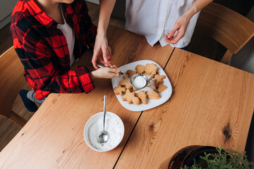 Mom and son are making cookies at a wooden table in the kitchen. Cooking desserts at home. Joint activities with children. Sprinkling cookies with powdered sugar. Top view
