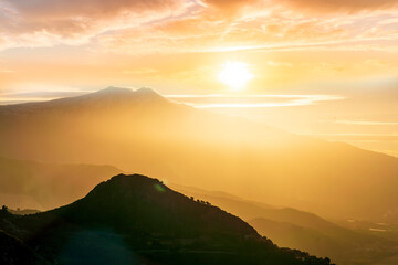 mysterious landscape of great erupting volcano with smoke from craters , clouds of gas and snow on slopes in orange light of sunset. eruption of vulcan
