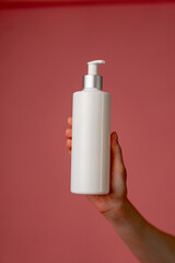 close up studio beauty shoot on a pink background female hands holding a white container with a dispenser for lotion beauty industry beauty salons