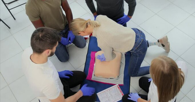 Group of people learning how to make first aid heart compressions with dummies during the training indoors.