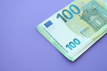 Big amount of one hundred euro money bills on lilac background