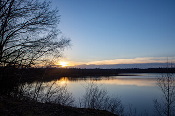 Obraz premium A tranquil sunset with vibrant reflections on a still lake, framed by bare trees and distant mountains