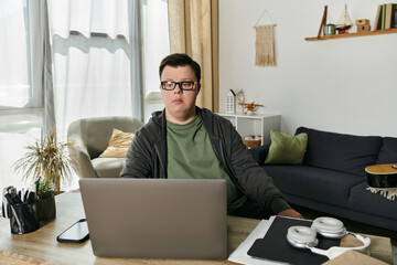A young man with Down syndrome engages in an online learning session in his cozy home.