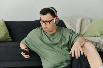 Obraz premium A young man with Down syndrome listens to music while sitting comfortably on a couch.