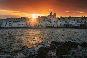 A picturesque view of Naoussa village in Paros Island, Greece, showcasing charming white-washed buildings with blue accents, narrow cobbled streets, and vibrant fishing boats in a crystal-clear harbor