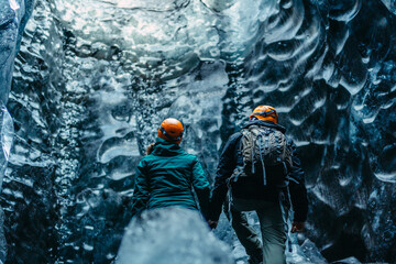 Equipped couple standing in ice cave in front of ice wall, Iceland