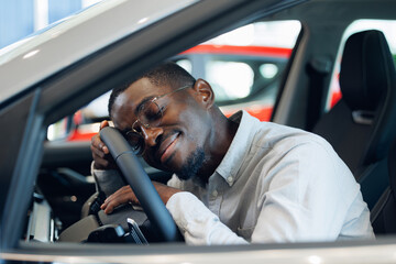 Happy African American man hugging steering wheel of his new car and smiling