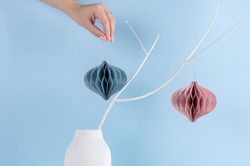 Christmas honeycomb paper decor on white branch on blue background. Seasonal holidays, interior, eco friendly holiday.