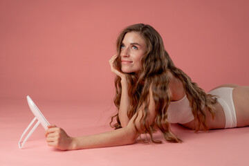studio beauty shoot on a pink background beautiful girl lying down looking in the mirror skin...