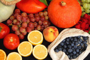 Round straw bag and various seasonal fruits and vegetables on dark background. Summer and fall produce. Selective focus.