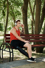 Fototapeta premium A young man with tattoos sits on a bench outdoors, enjoying the music in headphones.