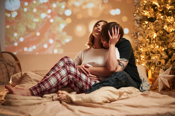 With decorated fir tree. Beautiful young couple indoors, celebrating new year against projector