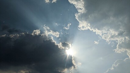 A dramatic sky with a mix of dark gray and light blue clouds. The sun is shining brightly through a...