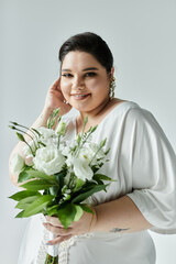 A radiant plus size bride holds a bouquet of white flowers while posing gracefully in her elegant dress.