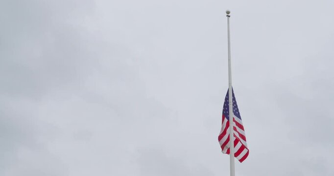American flag blowing in the wind at half mast or half staff. United States of America stars and stripes national flag moving slowly hanging halfway on flagpole symbolizing mourning or memorial day