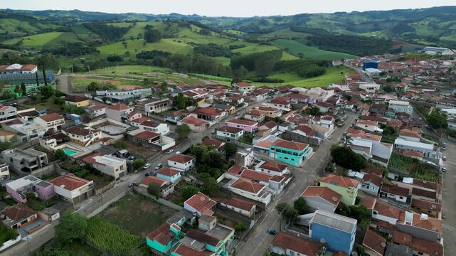 aerial view going down of a small neighborhood with orange roofs houses and lined streets surrounded by green hills - Bueno Brandao, Minas Gerais, Brazil
