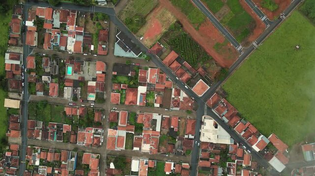 arial view going down rotating - a neighborhood with red roof houses surrounded by green hills during a cold foggy day - Bueno Brandao, Minas Gerais, Brazil