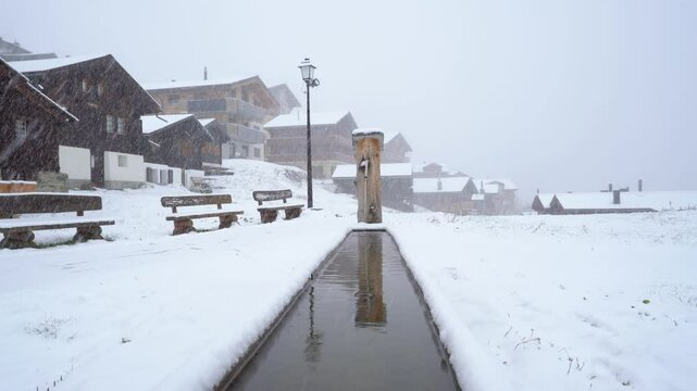 A water fountain in a small winter village in the snow. Frozen landscape on the Bettmeralp in Switzerland - static shot