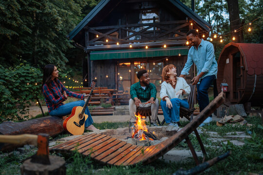 Friends enjoying a campfire in front of a cabin - Powered by Adobe