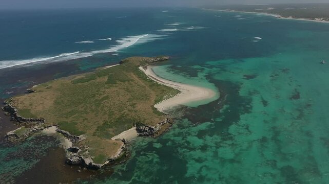 Aerial over Lancelin island showing the shallow blue waters and surrounding coral reef, descending and panning towards the beach.