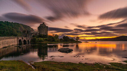 Fototapeta premium Langzeitbelichtung des Eilean Donan Castle, Spiegelung bei Sonnenuntergang im Loch Duich, orange und lila Wolken erzeugen eine mystische Stimmung