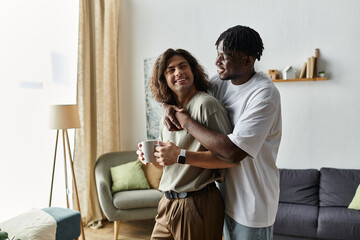 Two partners share a warm embrace while laughing, sipping coffee, and enjoying their home.