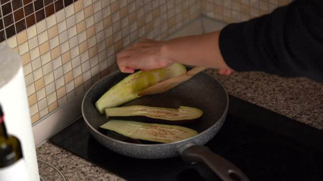 A young woman lays out sliced ​​eggplants on a pan for frying and cooking the southern classic parmigiana in the kitchen. The concept of home cooking, healthy eating, fresh vegetables