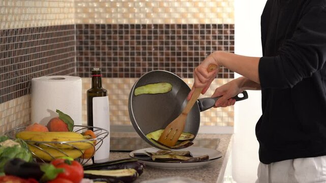 A young woman lays out fried and sliced ​​eggplants from a pan and cooking a southern classic dish parmigiana in the kitchen. The concept of home cooking, healthy eating, fresh vegetables