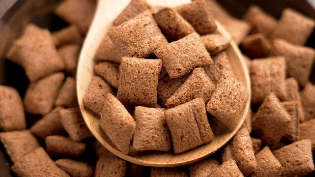 Brown corn cereal pillows with a rich chocolate crust in wooden spoon, capturing their crispy crunchy texture as a perfect breakfast. Top view. Rotation