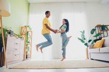 Photo of crazy cool positive multinational couple have fun jump up weekend vacation indoors flat apartment