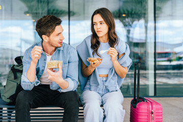Friends, Caucasian man and woman, eating snacks sitting at airport terminal, casually dressed in conversation luggage suggesting travelers. leisure, friendship, travel, relaxation during airport wait.