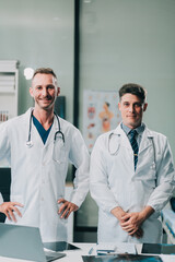 Portrait of two dedicated doctors smiling and looking at camera while holding a tablet and a diary in clinic. Two smiling doctors in white coat working in an office and looking at camera.