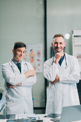 Portrait of two dedicated doctors smiling and looking at camera while holding a tablet and a diary in clinic. Two smiling doctors in white coat working in an office and looking at camera.