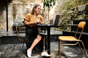 A young woman with an artificial limb sits comfortably in a cafe, sipping coffee while working on...