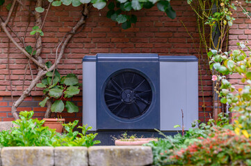 Air source heat pump unit installed on the exterior of residential house with brick wall backdrop. Sustainable heating solutions for old construction.