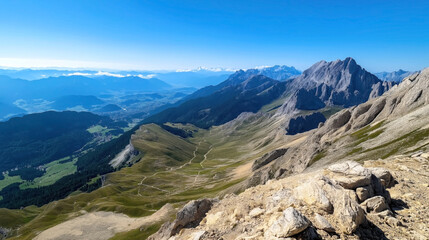 Expansive view of mountain range with rugged peaks and grassy valleys under a clear blue sky.