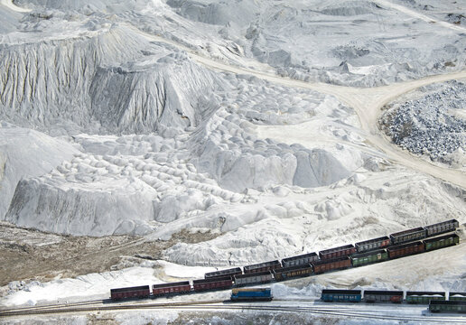 Aerial view of industrial mining operation with heavy machinery and a railway amidst hills and dust, Bashkortostan Republic, Russia.