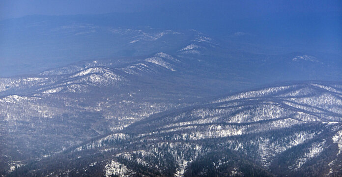Aerial view of majestic snow-covered mountains and lush forests in a serene winter landscape, Bashkortostan Republic, Russia.