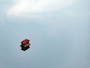Aerial view of a serene house with a red roof floating on calm water reflecting the blue sky, Sverdlovsk Oblast, Russia.