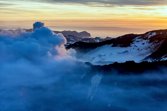 Aerial view of mutnovsky volcano at sunset surrounded by clouds and mountains, kamchatka peninsula, russia.