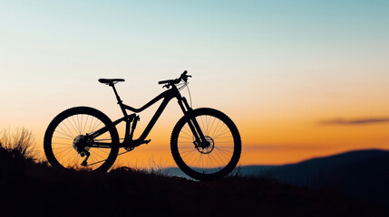 Obraz premium Silhouette of a mountain bike on a hill at sunset with an orange and blue sky in the background, emphasizing outdoor adventure and cycling.