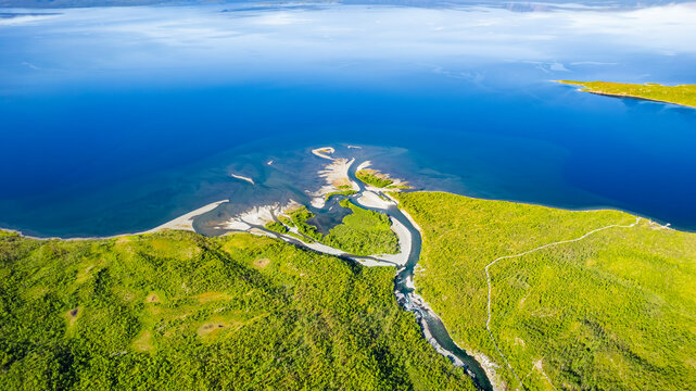 Aerial view of the serene delta of Abiskojakka River meeting the expansive Tornetrask Lake surrounded by lush forests, Abisko National Park, Sweden.