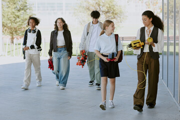 Young female teacher holding yellow robot and discussing it with blonde female student while rest of students carrying robots and smiling in background