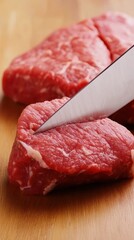 Fresh cuts of red meat on a wooden surface with a sharp knife.