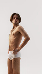 Young handsome man, posing in white underwear holding hands on hips and looking at distance seriously against white studio background. Concept of natural beauty, male health, fashion, skin care. Ad