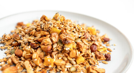 A bowl of granola with nuts and seeds on a white plate. The granola is a mix of different types of grains and nuts, and it looks like a healthy snack.