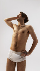 Obraz premium Low angle view of young man with defined muscles posing with arm lifted in relaxed posture against white studio background. Concept of natural beauty, male health, fashion, skin care. Ad