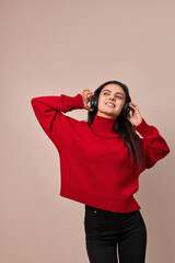Happy woman wearing red sweater and headphones enjoying listening music on pink background.