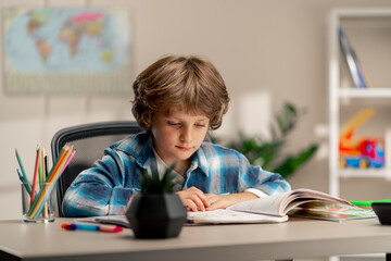 in the children's room a schoolboy in white sweater and a blue checkered shirt lies on a desk...