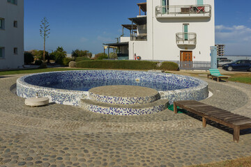 A serene pool surrounded by quaint buildings and lush landscaping on a bright sunny day.